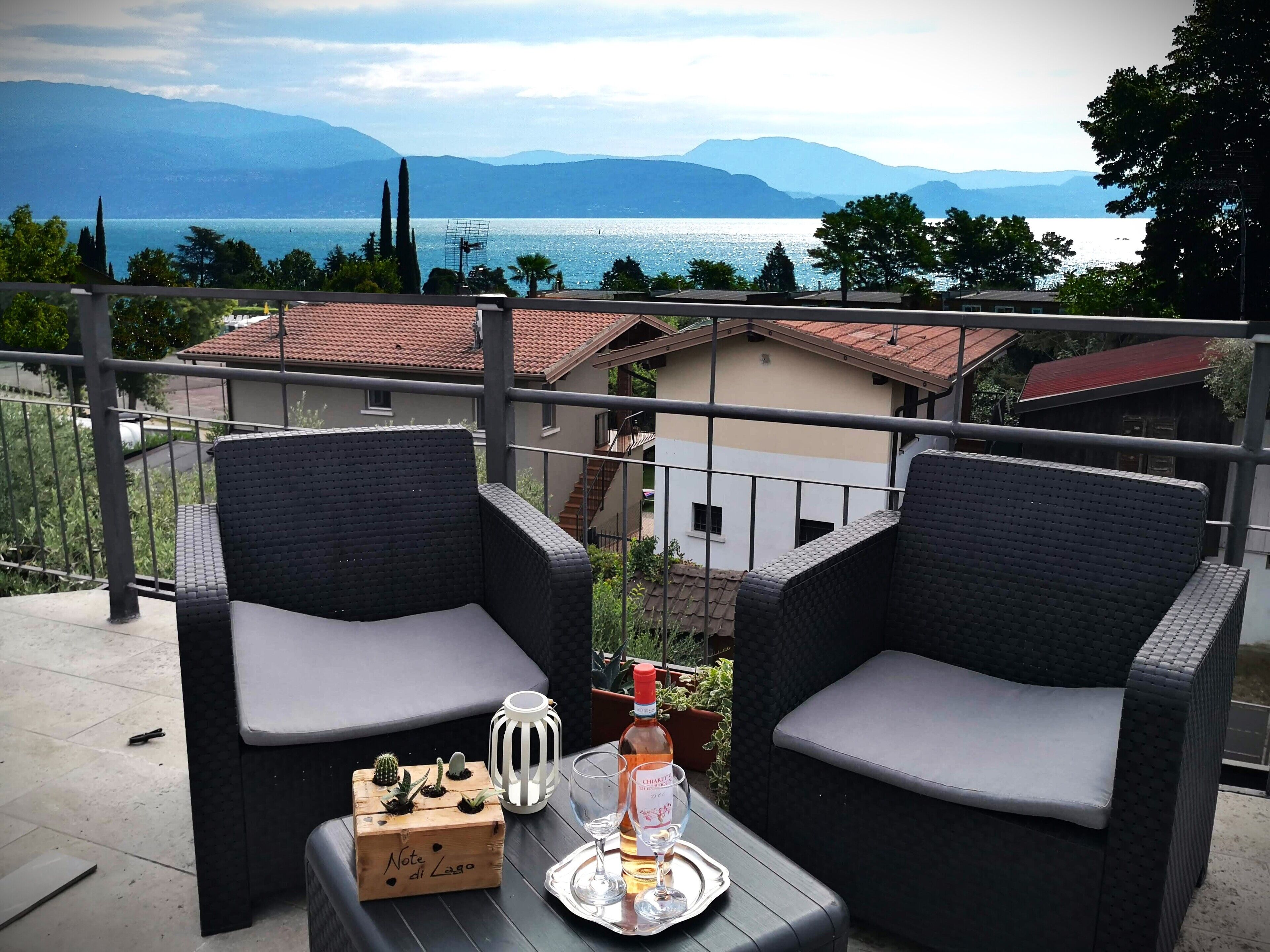 A balcony with wicker chairs, a small table, a bottle of Châteauneuf, and a box of cacti.