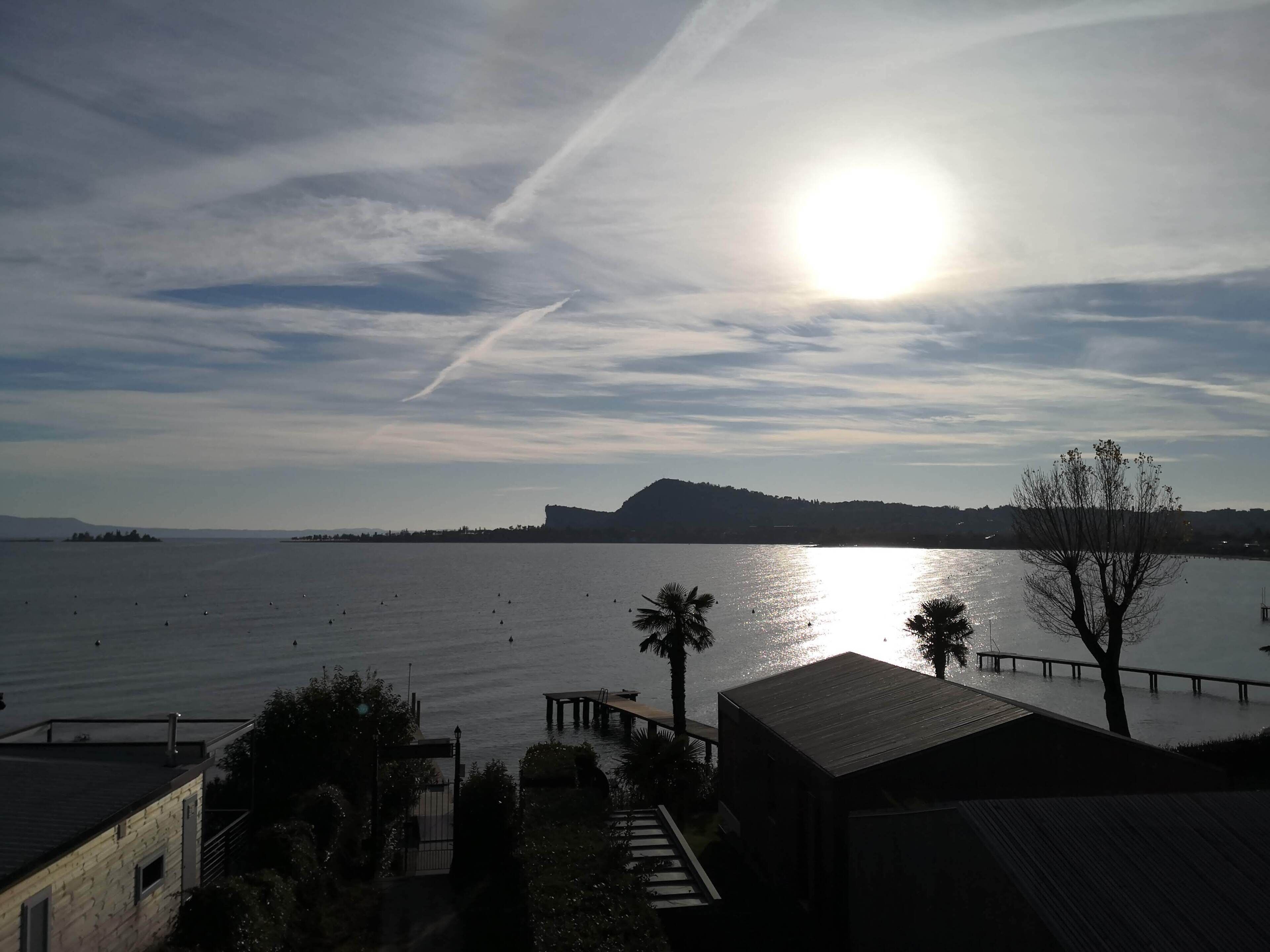 On aperçoit une étendue d ’eau calme, une terre ferme au loin, un quai en bois et un bâtiment doté d’un toit en pente.