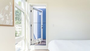Een slaapkamer met een groot raam, een bed en uitzicht op een blauw gebouw.