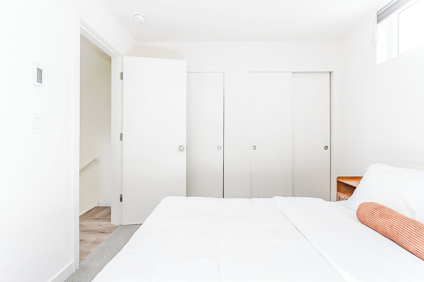 A modern bedroom with a bed, white walls, and a wooden floor.