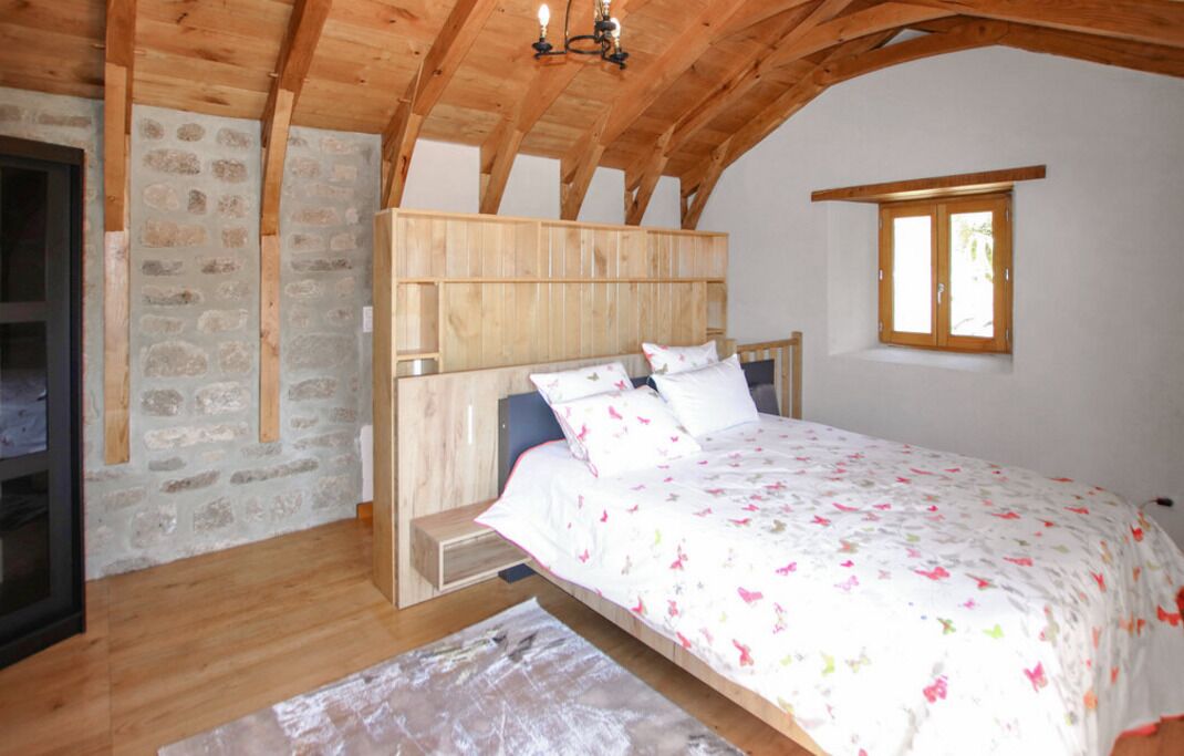 A bedroom with a wooden headboard, a bed with floral bedding, a stone wall, and a window with wooden shutters.
