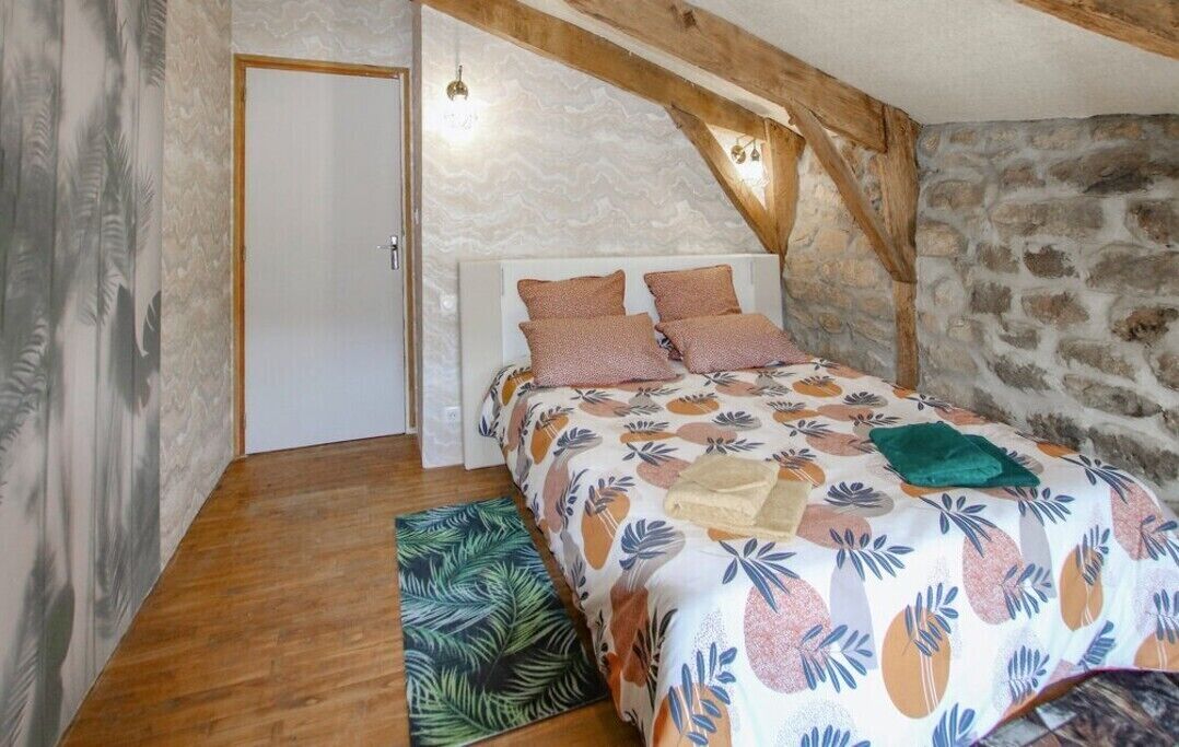 A bedroom with a bed, wooden beams, a stone wall, and a door.