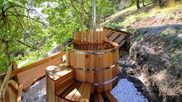 A wooden hot tub with benches, surrounded by gravel and trees.
