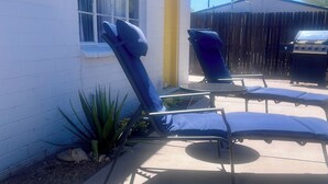 Een terras met twee ligbedden, een tafeltje en een barbecuehoek.