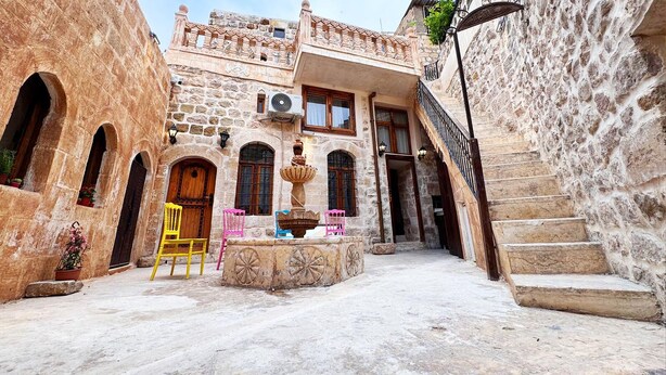A courtyard with a stone building, a fountain, and a staircase. - kefren konağı (Mardin)