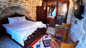 A room with a stone wall, a bed with a wooden headboard, a wooden chair, a mirror, and a television. - kefren konağı (Mardin)