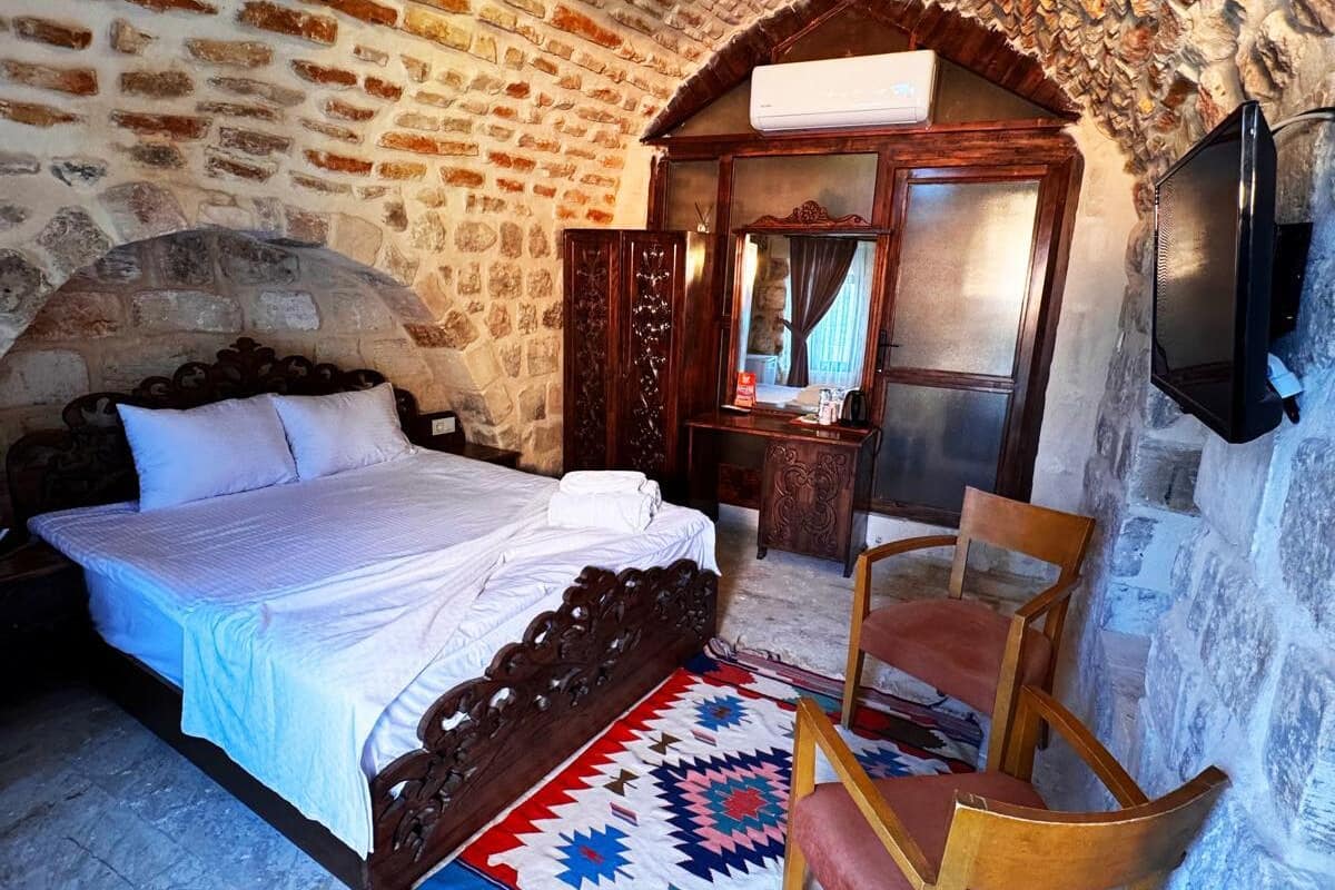 A bedroom with a stone wall, a wooden bed, a chair, a television, and a mirror.