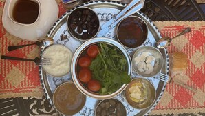 A traditional Middle Eastern meal served on a metal tray with various dishes including a stew, olives, tomatoes, and bread. - kefren konağı (Mardin)