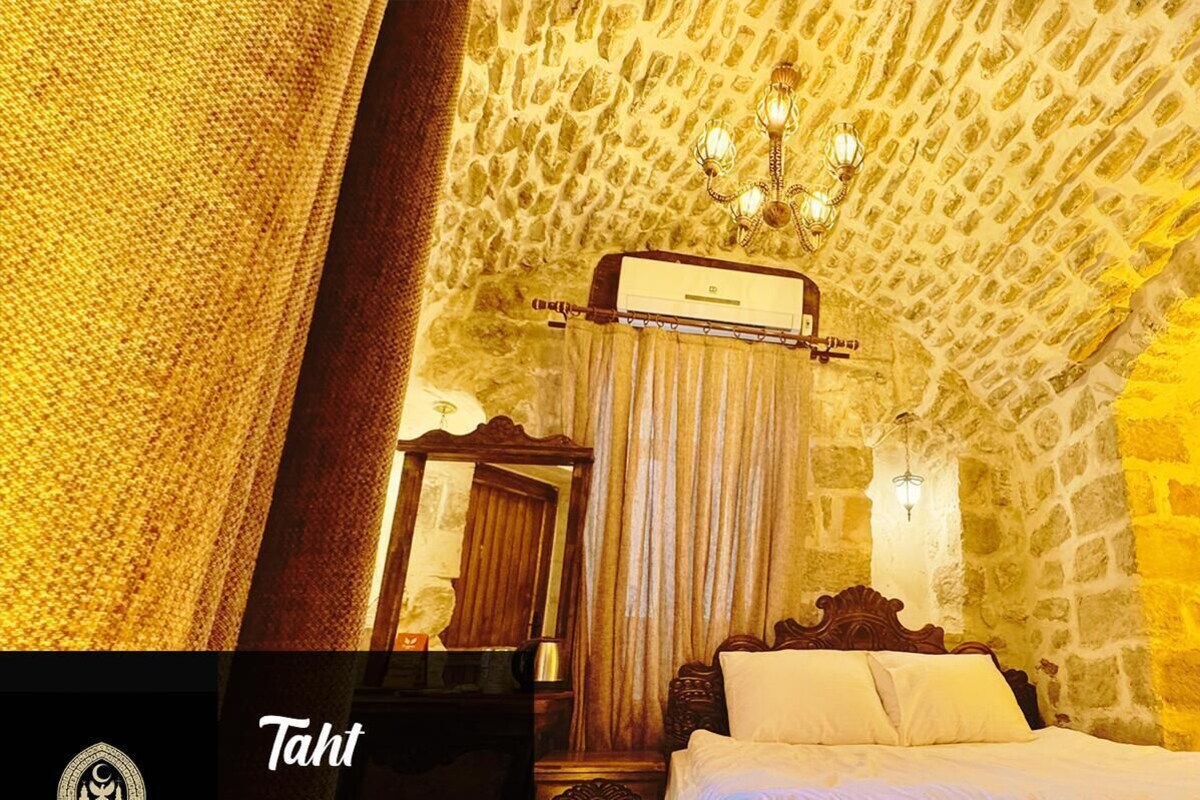 A room with a stone wall, a bed with white bedding, a wooden headboard, a mirror, and a chandelier.