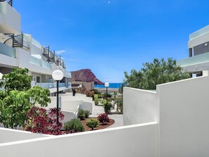 A modern hotel courtyard with a view of the sea and a mountain in the distance.