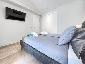 A modern bedroom with a bed, a flat-screen TV mounted on the wall, and a door with a towel rack.