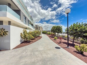 A modern building with a paved walkway, potted plants, and a clear sky.