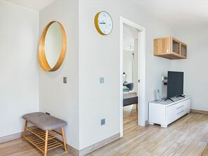 A modern room with a wooden bench, a round mirror, a clock, a television, and a cabinet.