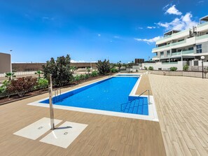 A rectangular swimming pool with a tiled deck surrounding it, a lifeguard stand, and a clear blue sky.