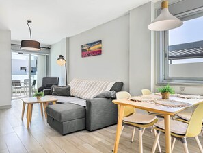 A modern living room with a sofa, a dining table with chairs, a pendant light, and a painting on the wall.