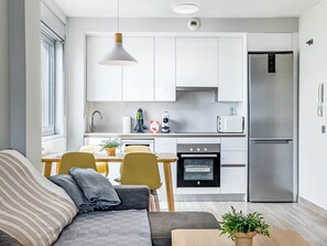 A modern kitchen with white cabinets, a stainless steel refrigerator, a built-in oven, and a dining area with a table and chairs.