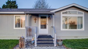 A single-story house with a front porch, a cross on the wall, and a small garden area with a wooden stump and a birdhouse. - 3BR Retreat in Prosser Perfect for Wine Lovers (Prosser)