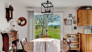 A dining room with a large wooden table and chairs, a wooden cabinet, a wall clock, and a view of a green landscape through a glass door. - 3BR Retreat in Prosser Perfect for Wine Lovers (Prosser)