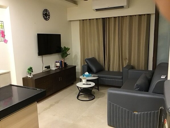 A modern living room with a flat-screen TV, a sofa, a coffee table, and a dining area.