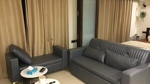 Una camera d'albergo moderna con un divano grigio, due tavolini rotondi e un letto sullo sfondo.