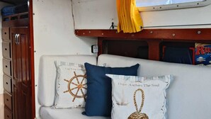 Een cabinterieur met een wit gestoffeerde bank, twee decoratieve kussens, een geel gordijn en een raam met uitzicht op een gebouw.