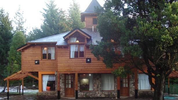 A two-story wooden house with a stone foundation, multiple windows, and a covered porch.