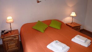 A bed with orange bedding, two green pillows, two bedside lamps, and two folded white towels.