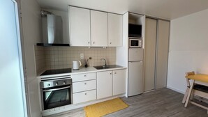 Een kleine keuken met witte kastjes, een magnetron, een koelkast, een fornuis en een spoelbak.