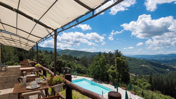 Un área junto a la piscina con mesas y sillas de madera, piscina y vistas a las montañas.