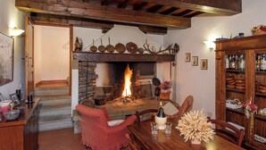 Una habitación acogedora con chimenea, vigas de madera, una mesa de comedor con sillas y un aparador con vajilla.