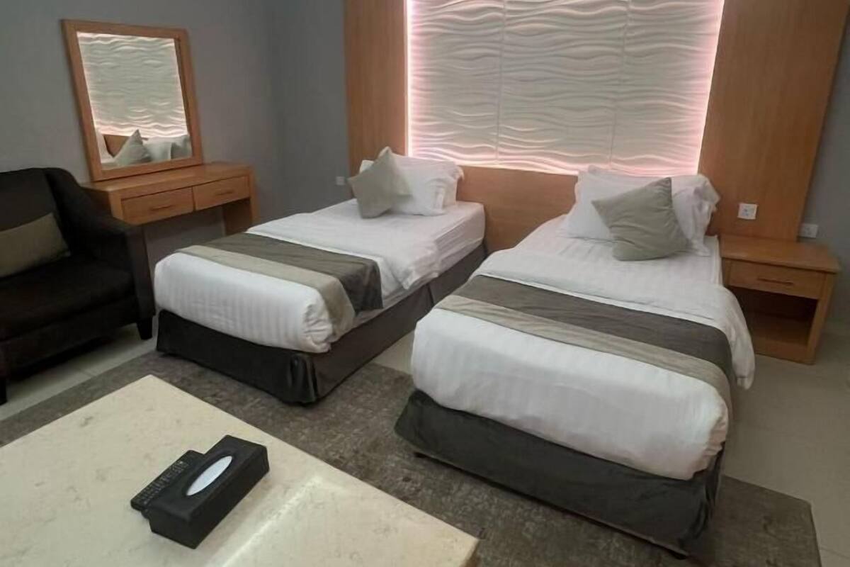 A hotel room with two beds, a desk, a chair, and a mirror.