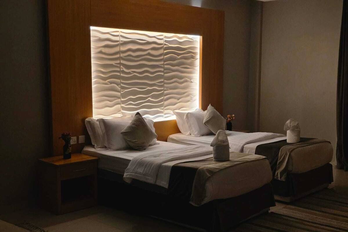 A hotel room with a large bed, a bedside table, and a wall-mounted light fixture.