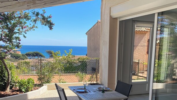Eine überdachte Terrasse mit Tisch und Stühlen, mit Blick auf die Küste.