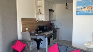 Ein modernes Wohnzimmer mit grauem Sofa und Sesseln, einer Küchenzeile mit weißen Schränken und einem Esstisch.