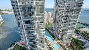 A high-rise building with a glass facade, a swimming pool, and a marina in the background. - Sun, Style & Skyline | Modern Icon Brickell 2BR (Miami)