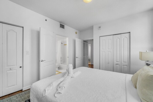 A hotel room with a large bed, white walls, and multiple doors leading to other rooms.