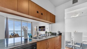 A modern kitchen with wooden cabinets, a stainless steel sink, and a dining area with white chairs. - City-View Retreat in Brickell 2BR + Free Parking (Miami)