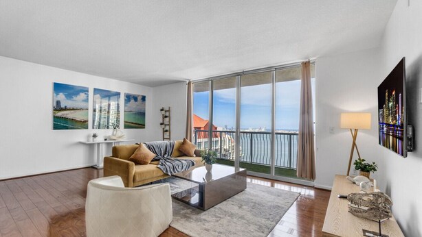A modern living room with a sofa, a coffee table, and a view of the city through large windows. - City-View Retreat in Brickell 2BR + Free Parking (Miami)