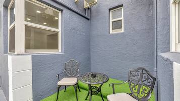 Un petit patio d’angle avec une table ronde et deux chaises, entouré de gazon synthétique.