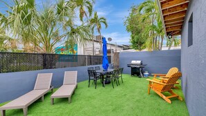 A patio with artificial grass, a table with chairs, a grill, and lounge chairs. - Studio off Las Olas- Steps to the Beach (Fort Lauderdale)