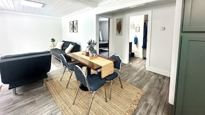 A modern living room with a dark sofa, a wooden dining table with chairs, and a woven rug.