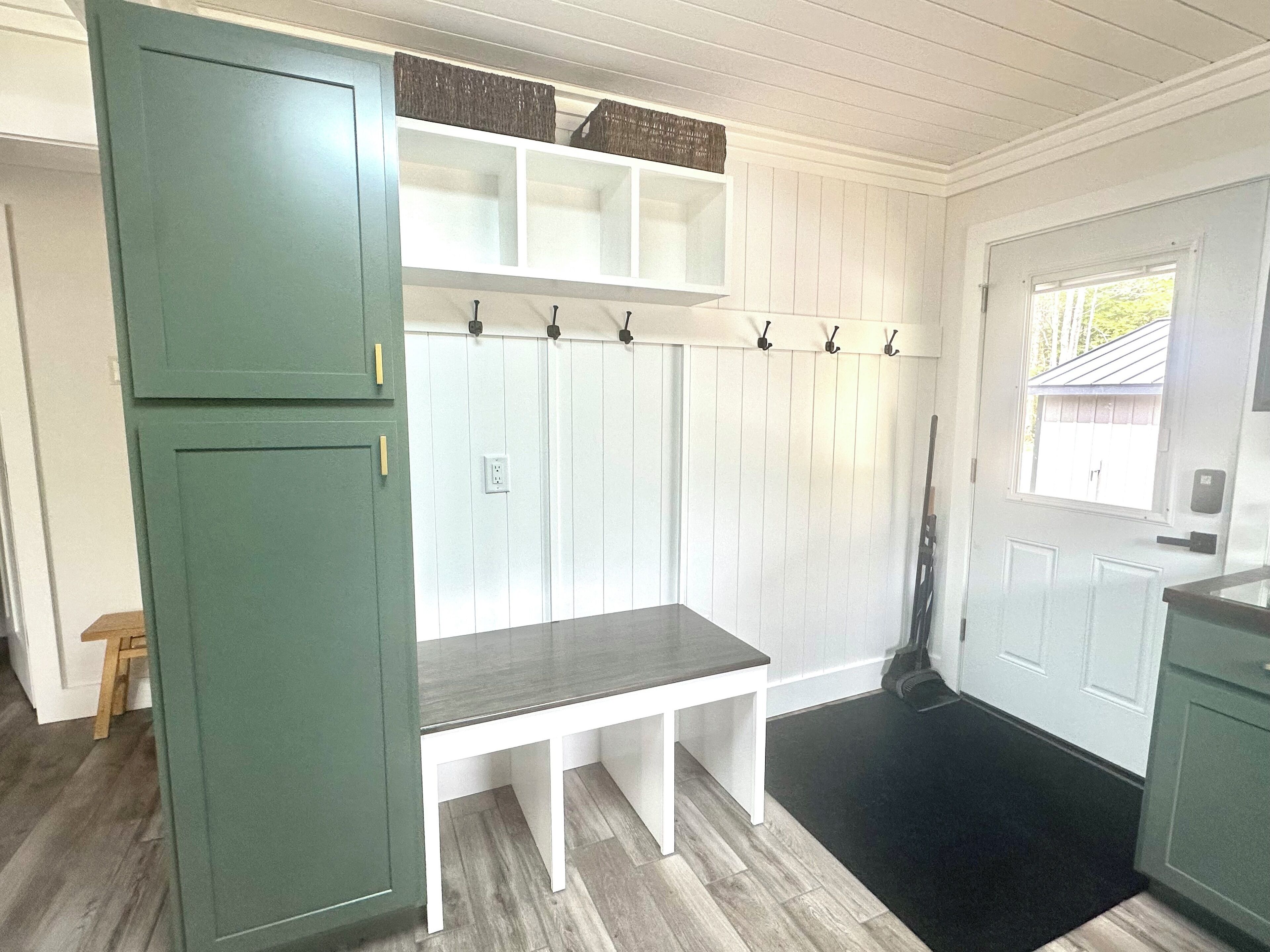 Une cuisine avec un meuble vert, un banc blanc et une porte avec une fenêtre.