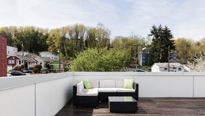 A rooftop terrace with a wicker sofa and ottoman, surrounded by a wooden deck and white walls. - North Beacon Hill Townhouse — 3 Bedrooms, Each with a Private En-Suite Bathroom (Seattle)