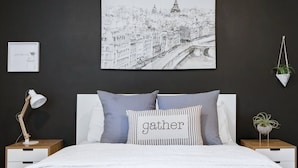 A neatly arranged bedroom with a bed, pillows, a bedside table with a lamp, a framed picture, and a hanging plant. - North Beacon Hill Townhouse — 3 Bedrooms, Each with a Private En-Suite Bathroom (Seattle)