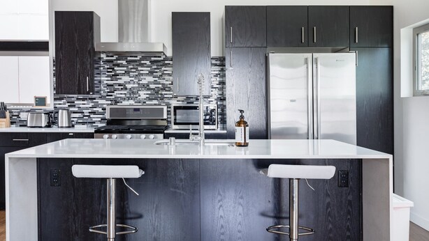 A modern kitchen with dark wood cabinets, a white island with bar stools, stainless steel appliances, and a black and white backsplash. - North Beacon Hill Townhouse — 3 Bedrooms, Each with a Private En-Suite Bathroom (Seattle)