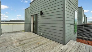 Ein modernes Gebäude mit grauer Fassade, einer Holzterrasse und einem Metallgeländer.
