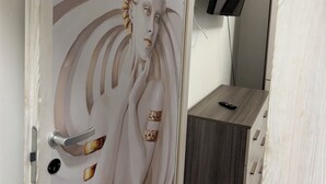 Habitación con una puerta decorativa que muestra el rostro de una mujer, un televisor de pantalla plana en la pared y un mueble de madera con cajones.