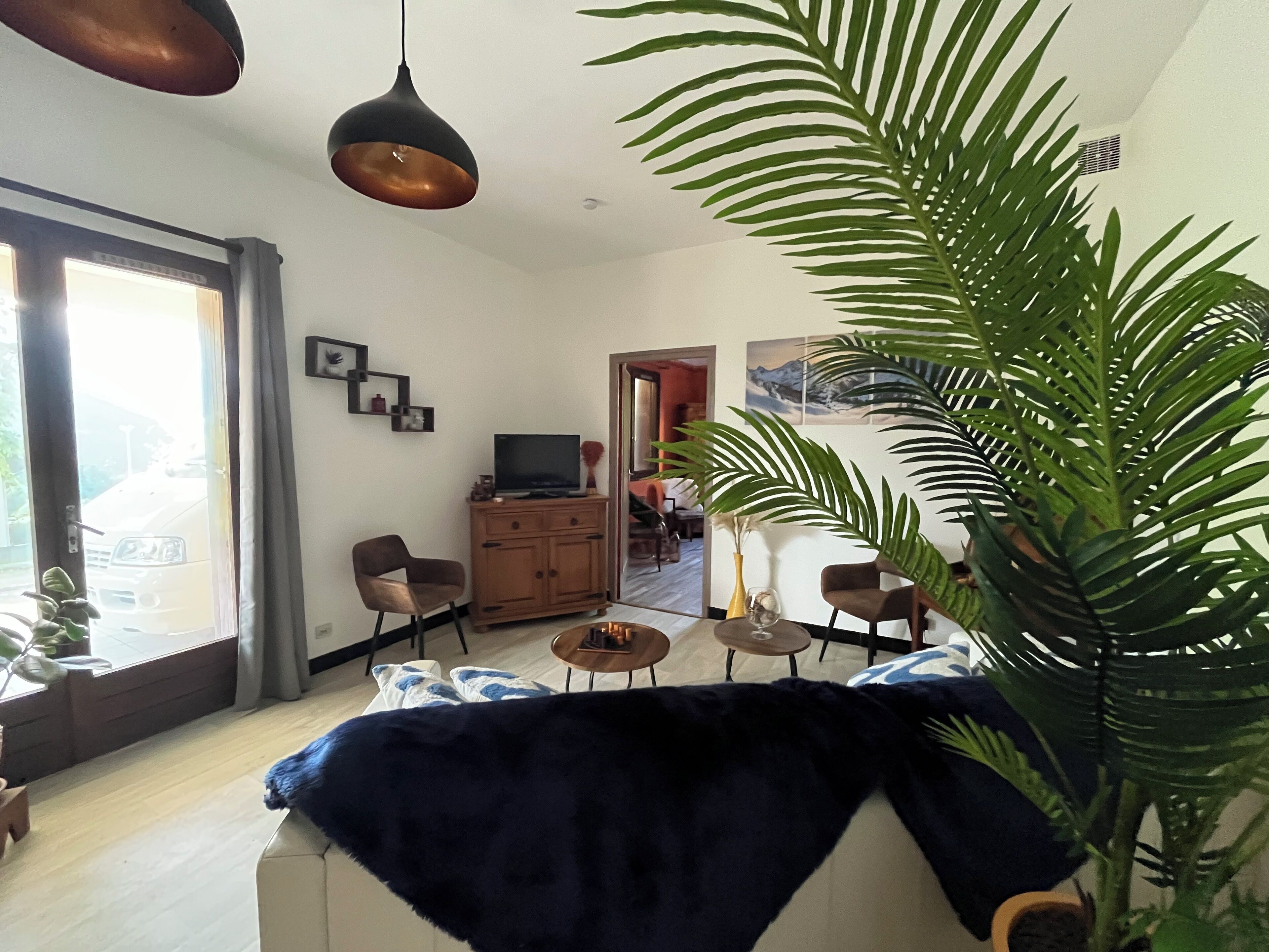 Ein Wohnzimmer mit einer Couch, einem Couchtisch, einem Fernseher auf einer Holzkommode und einer großen Pflanze.