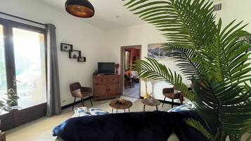 Ein Wohnzimmer mit einer Couch, einem Couchtisch, einem Fernseher auf einer Holzkommode und einer großen Pflanze.