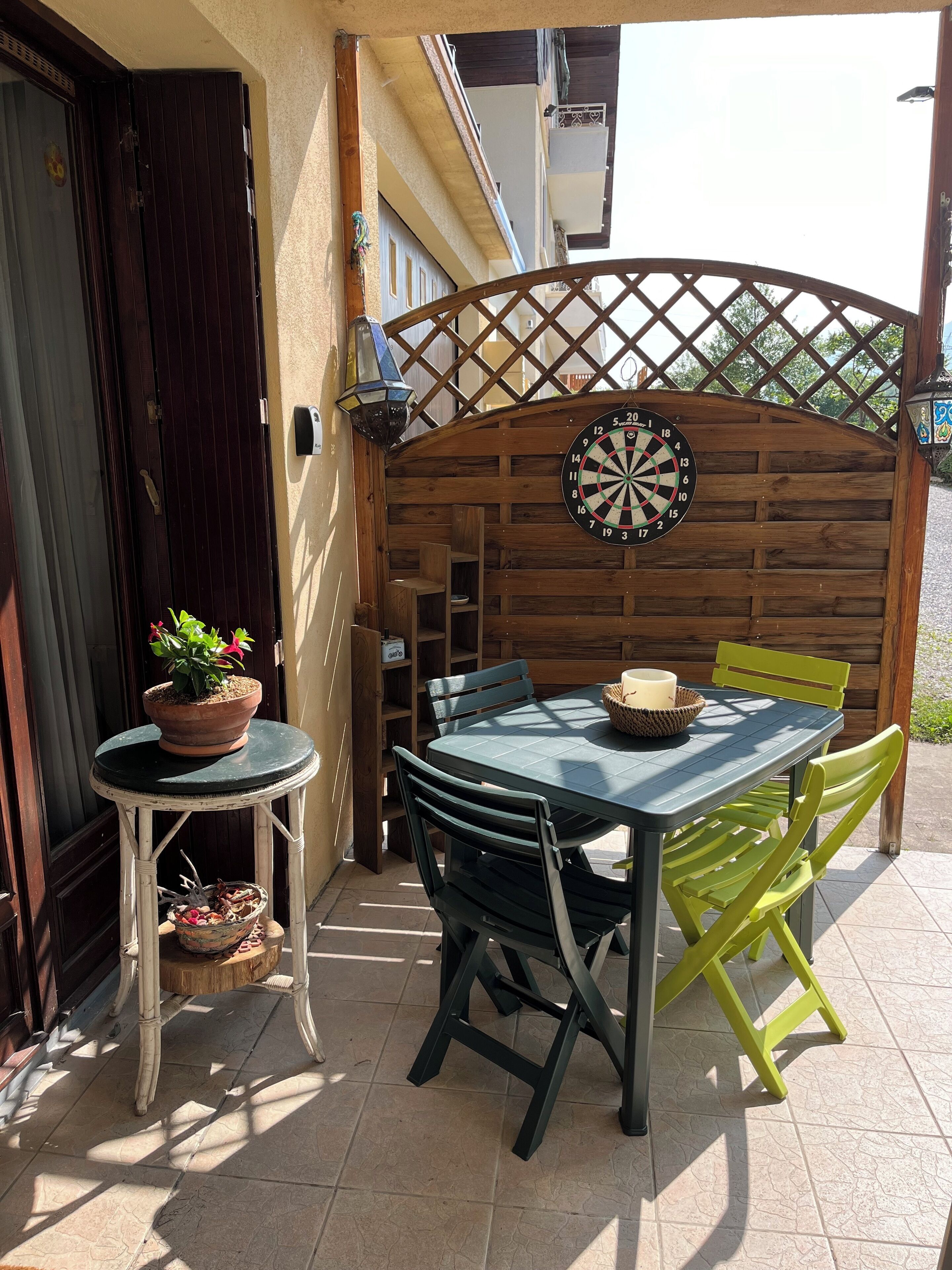 A patio area with a table and chairs, a potted plant, a dartboard, and a wooden lattice structure.